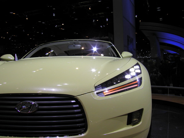 vůz v autosalonu, bílý Hyundai pohled zepředu, svítí světla.